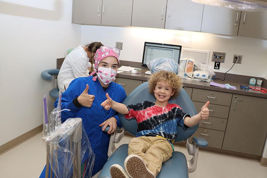 A kid sitting in a dental chair doing thumbs up with a hygienist to the right